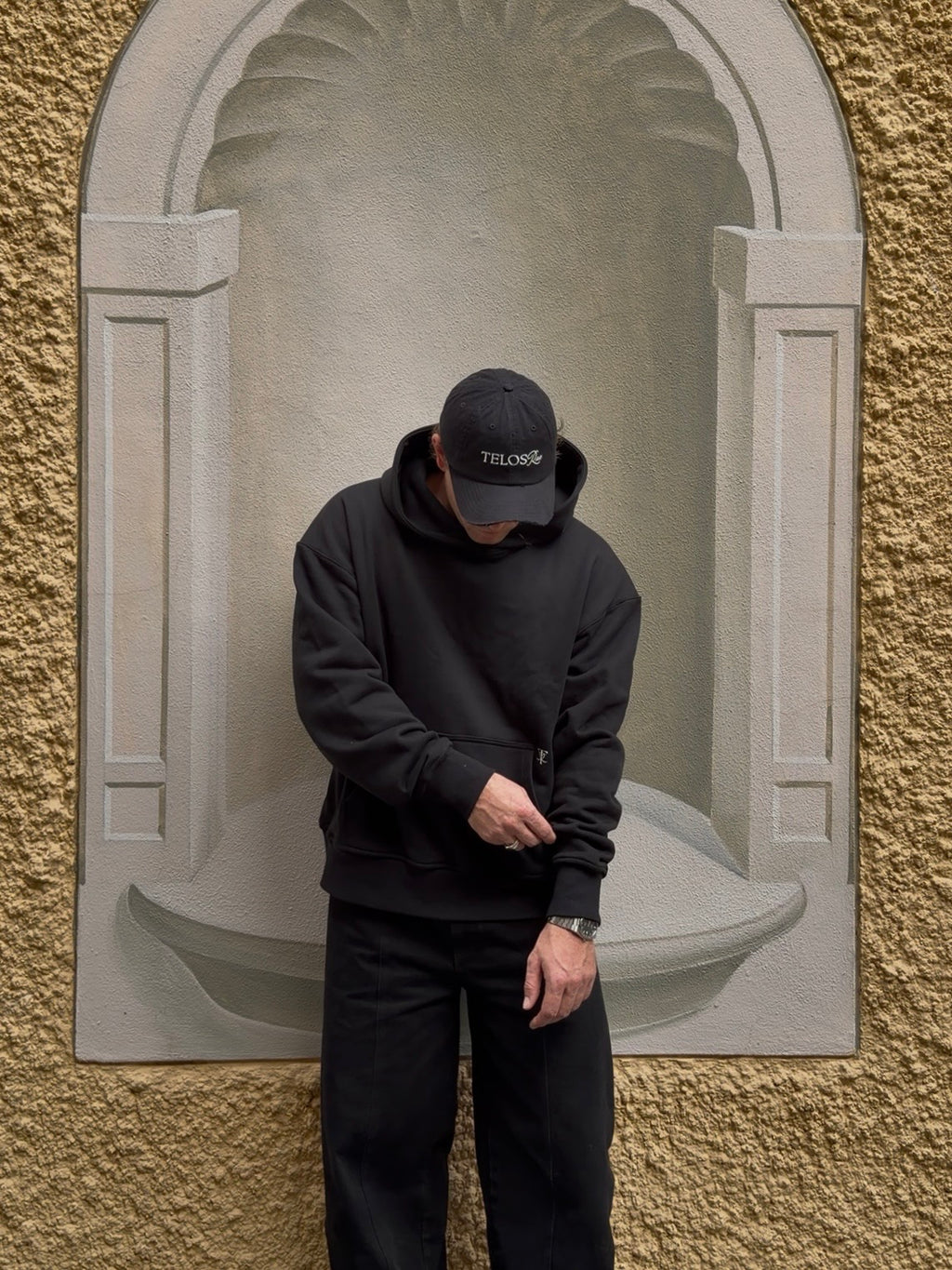 Model wearing the Telos Rae Box Hoodie in black, heavyweight organic cotton